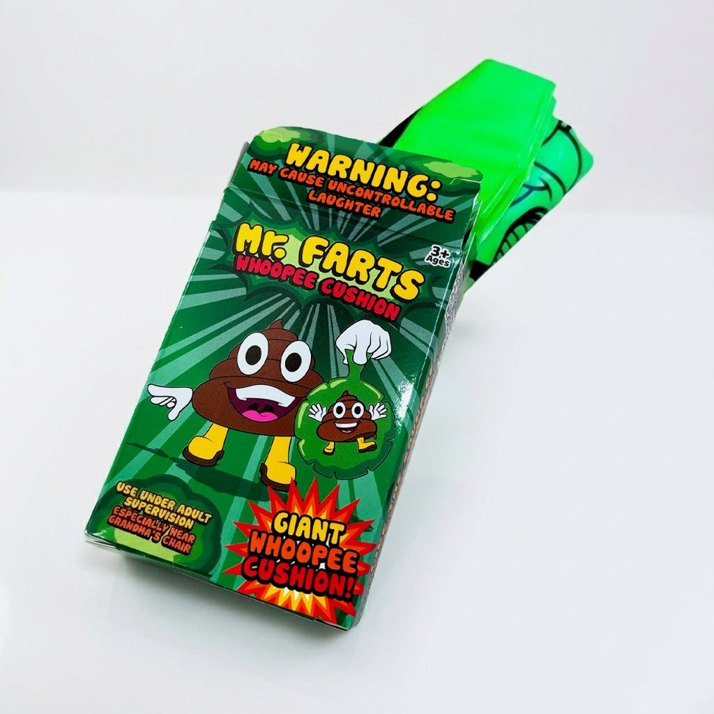 A giant green Mr farts Whoopee cushion folded up, coming out of it's packaging on a clean background with a Mr Farts Giant Whoopee Cushion packaging box open facing camera. 