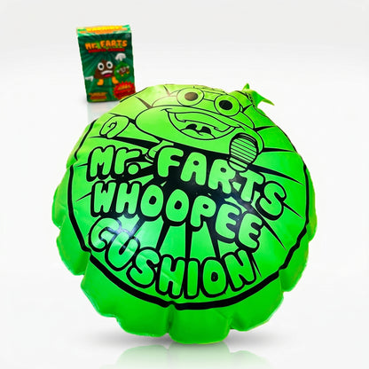 A giant green Mr farts Whoopee cushion centred on a clean background with a Mr Farts Giant Whoopee Cushion packaging slightly blurred behind it.