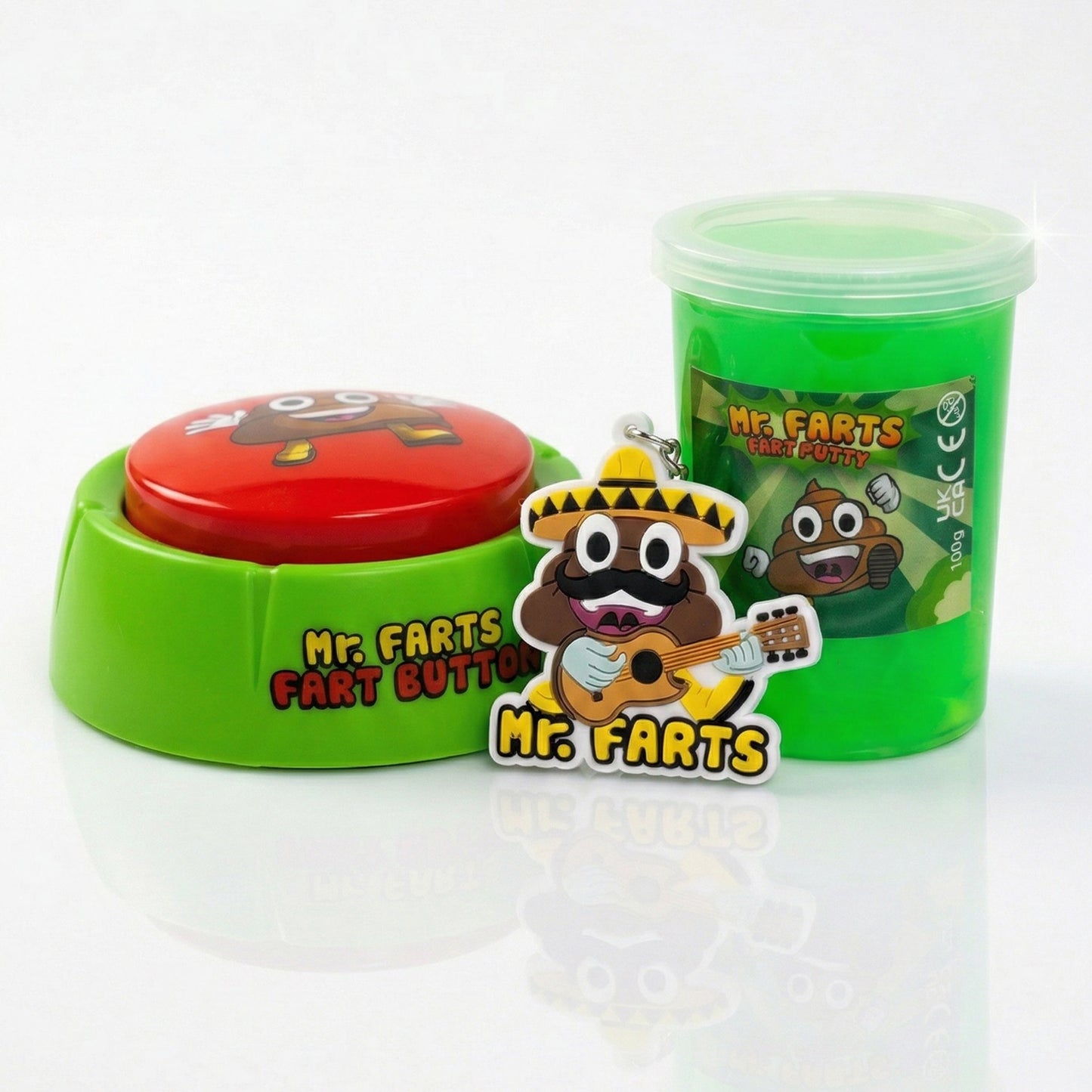 A novelty toy set featuring a green plastic tub of Fart Putty slime with a cartoon poop character on the label called Mr Farts, a Fart Button with green base and a red round button labeled 'Mr. Farts Fart Button,' and a matching cartoon Taco Farts keyring in front.